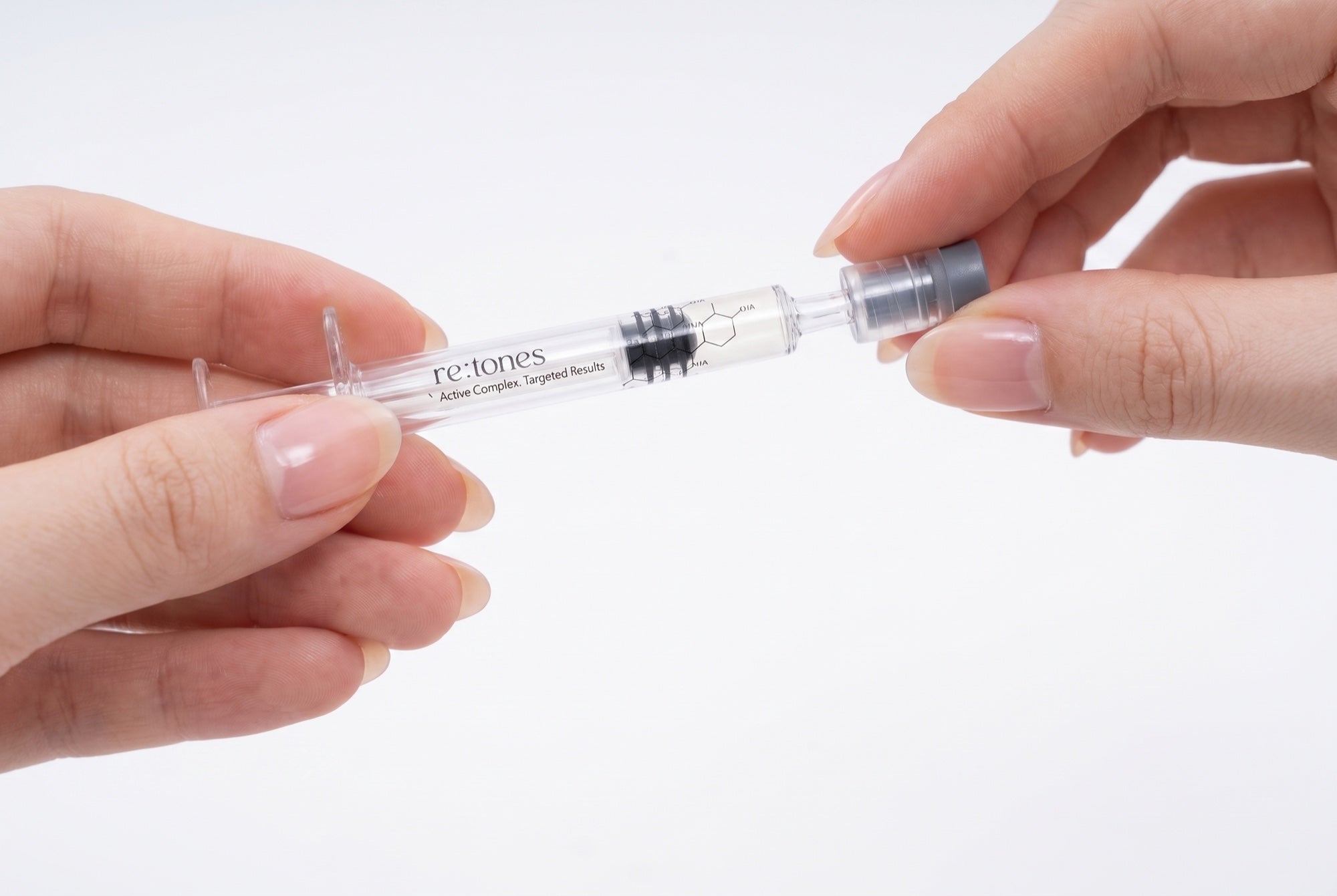 Two hands pulling the gray protective cover off the tip of the re:tones ampoule applicator