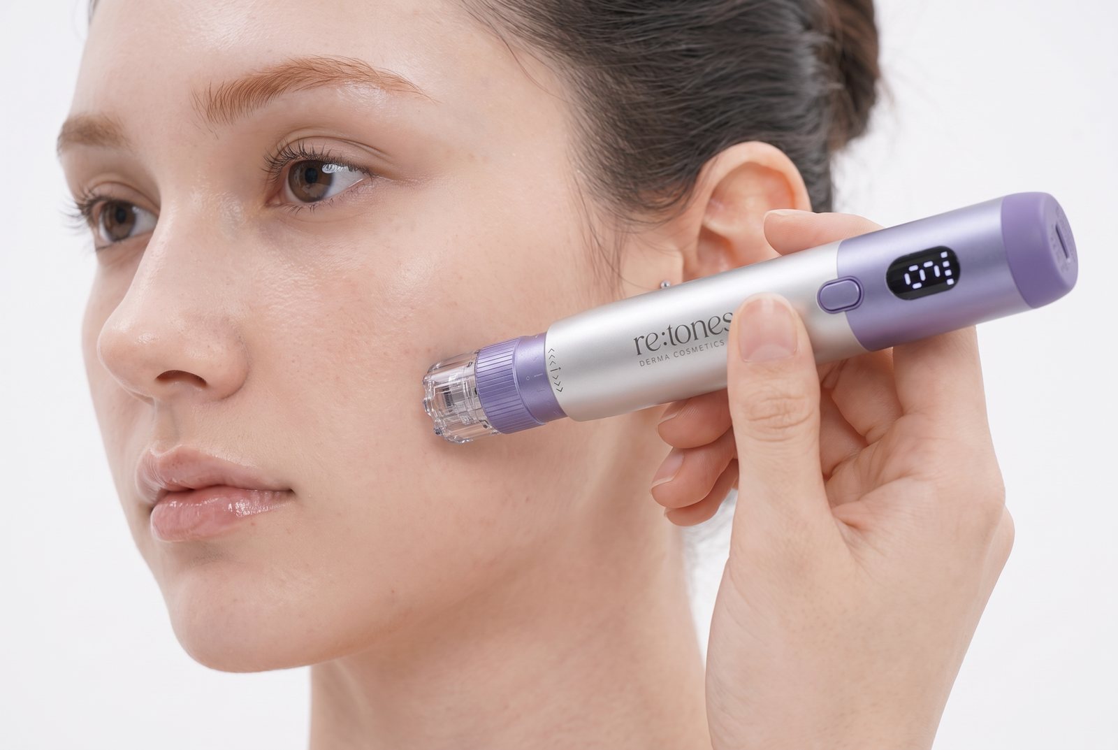 The re:tones Skin Rejuvenation Tap Pen Device pen held against a cheek, the cartridge flat on the skin.