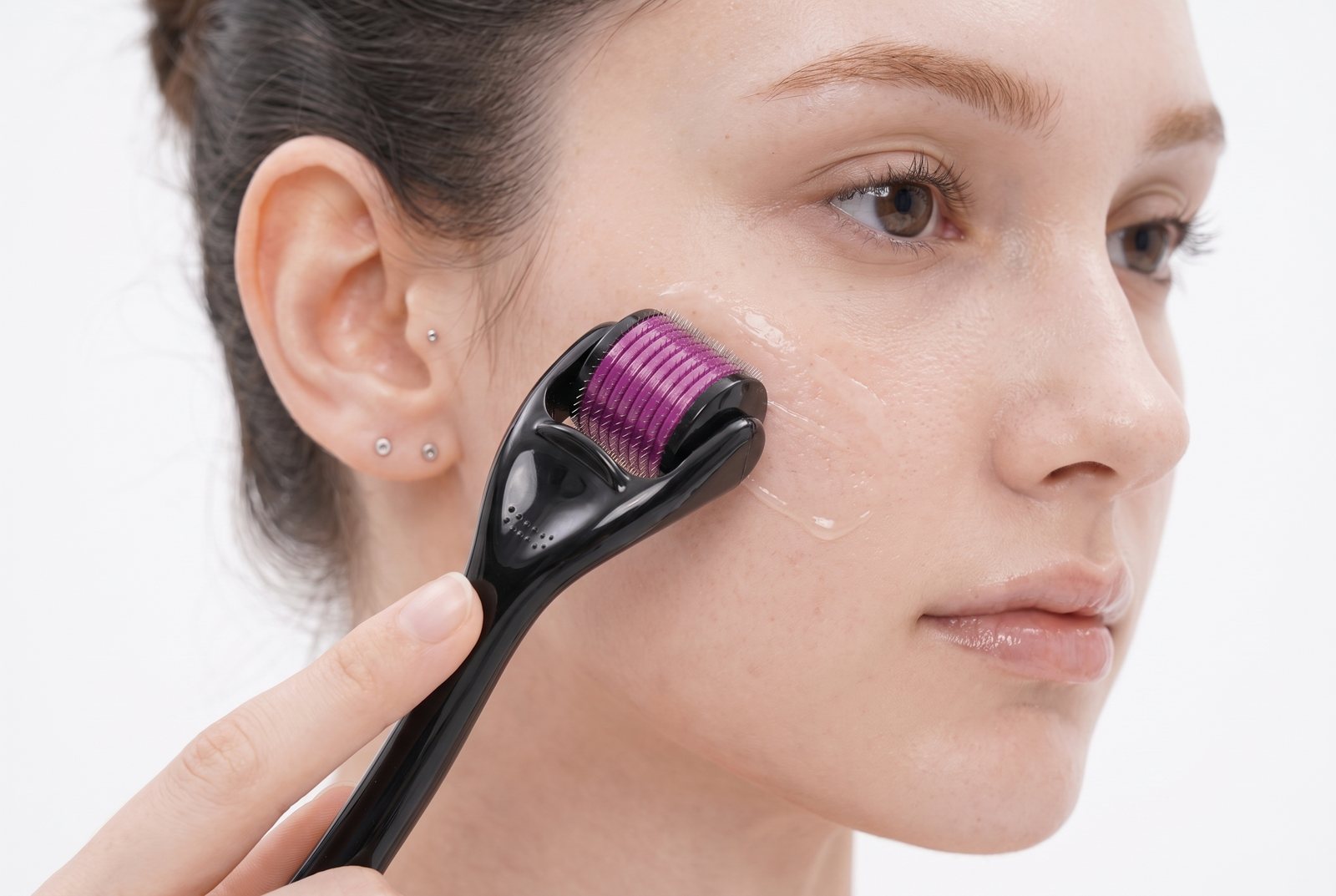 A manual derma roller held against a cheek, the drum resting on the skin.